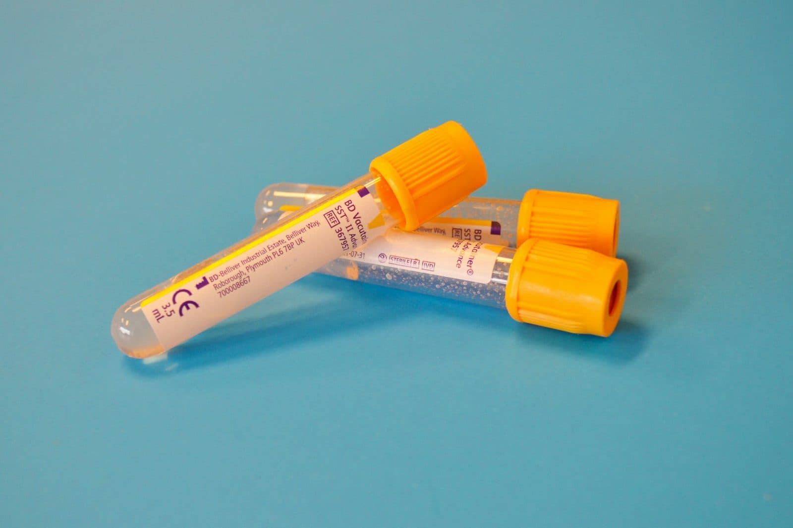 Gold-capped blood collection tubes of the kind used for liver function tests, lying on a blue surface.