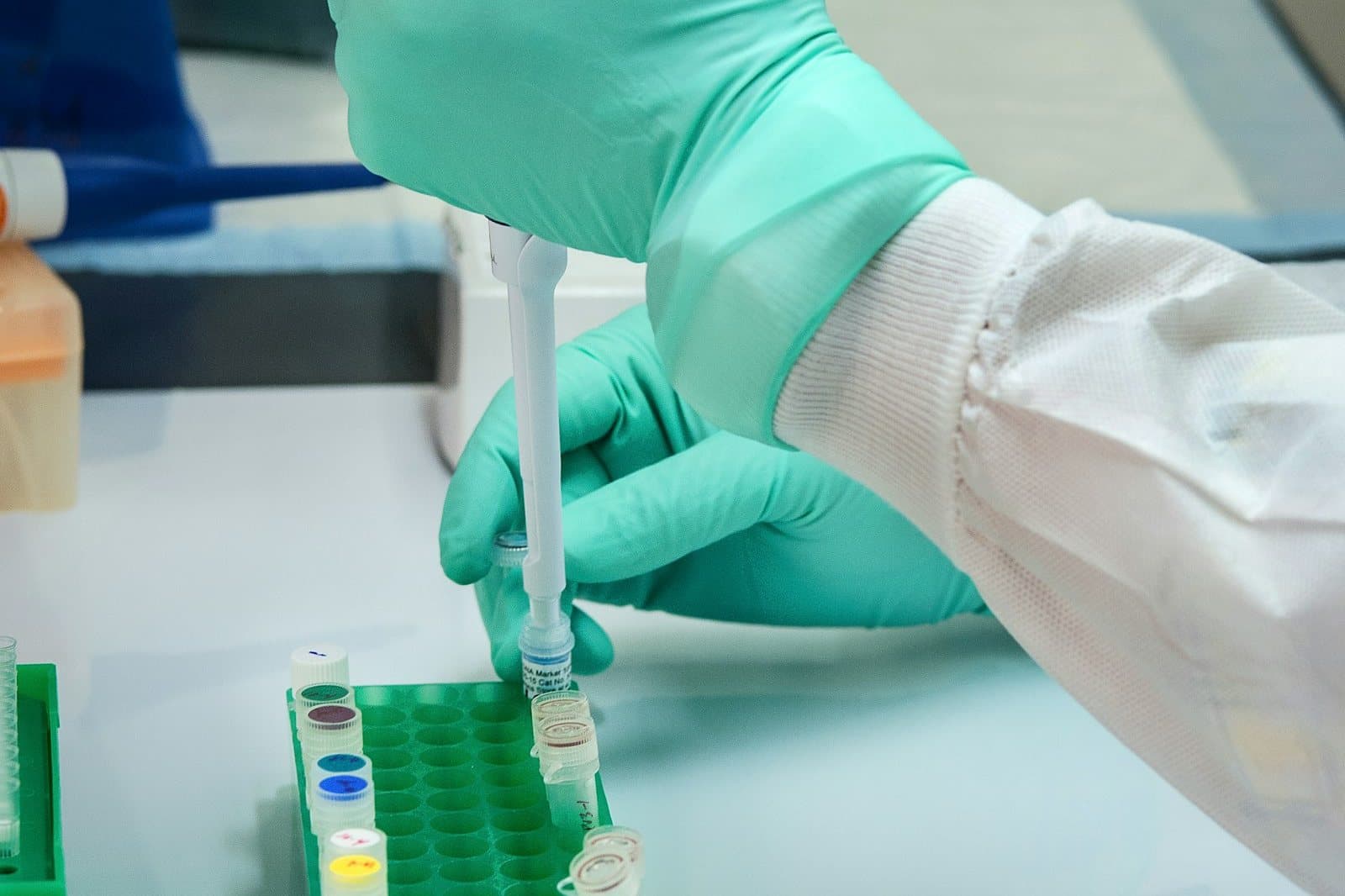 Gloved hands pipetting a sample into a tube rack in a lab, the first step of the gene tests run at an AML diagnosis.