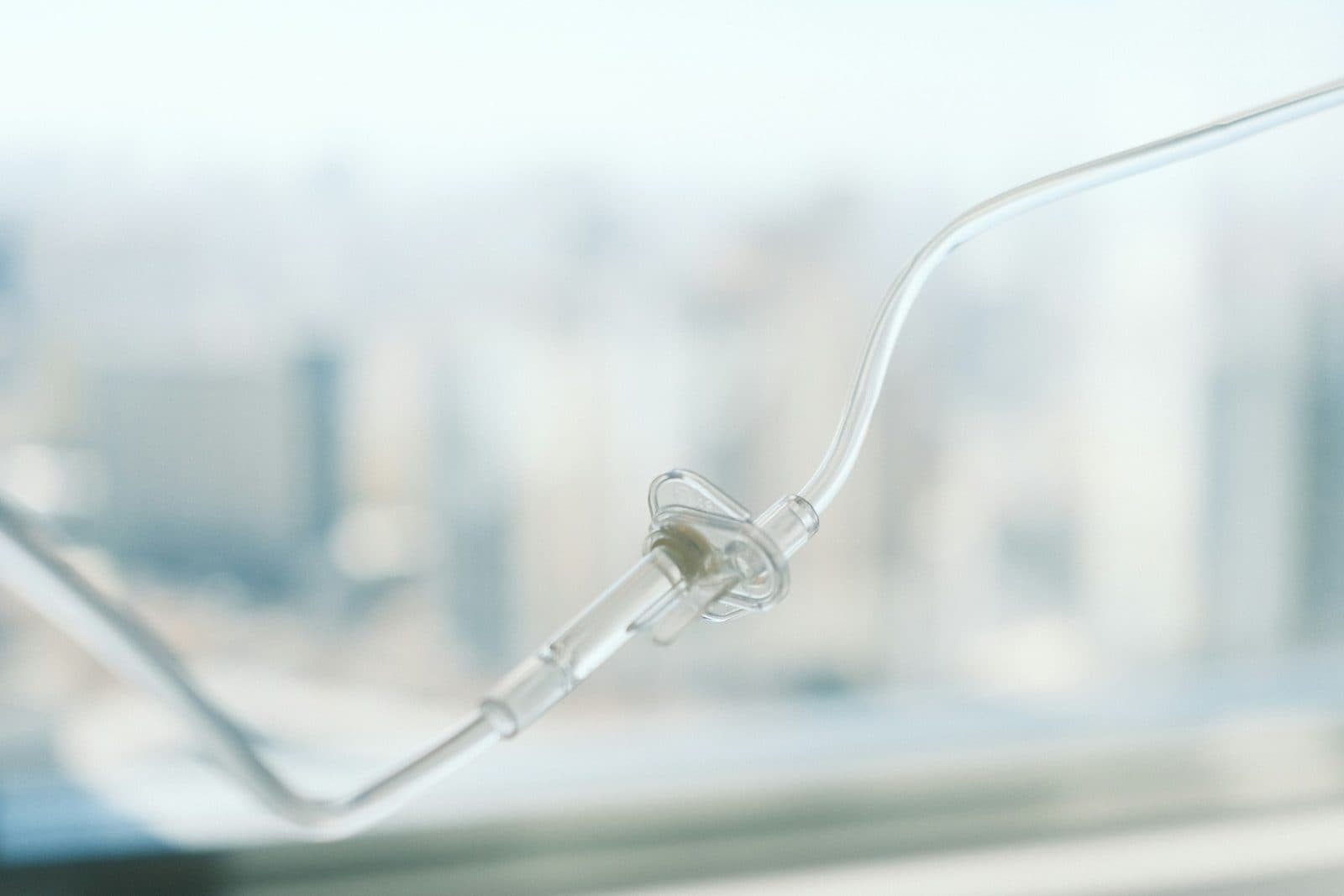 A clear IV infusion line in soft focus against a bright window, the way Gaucher enzyme infusions are given.