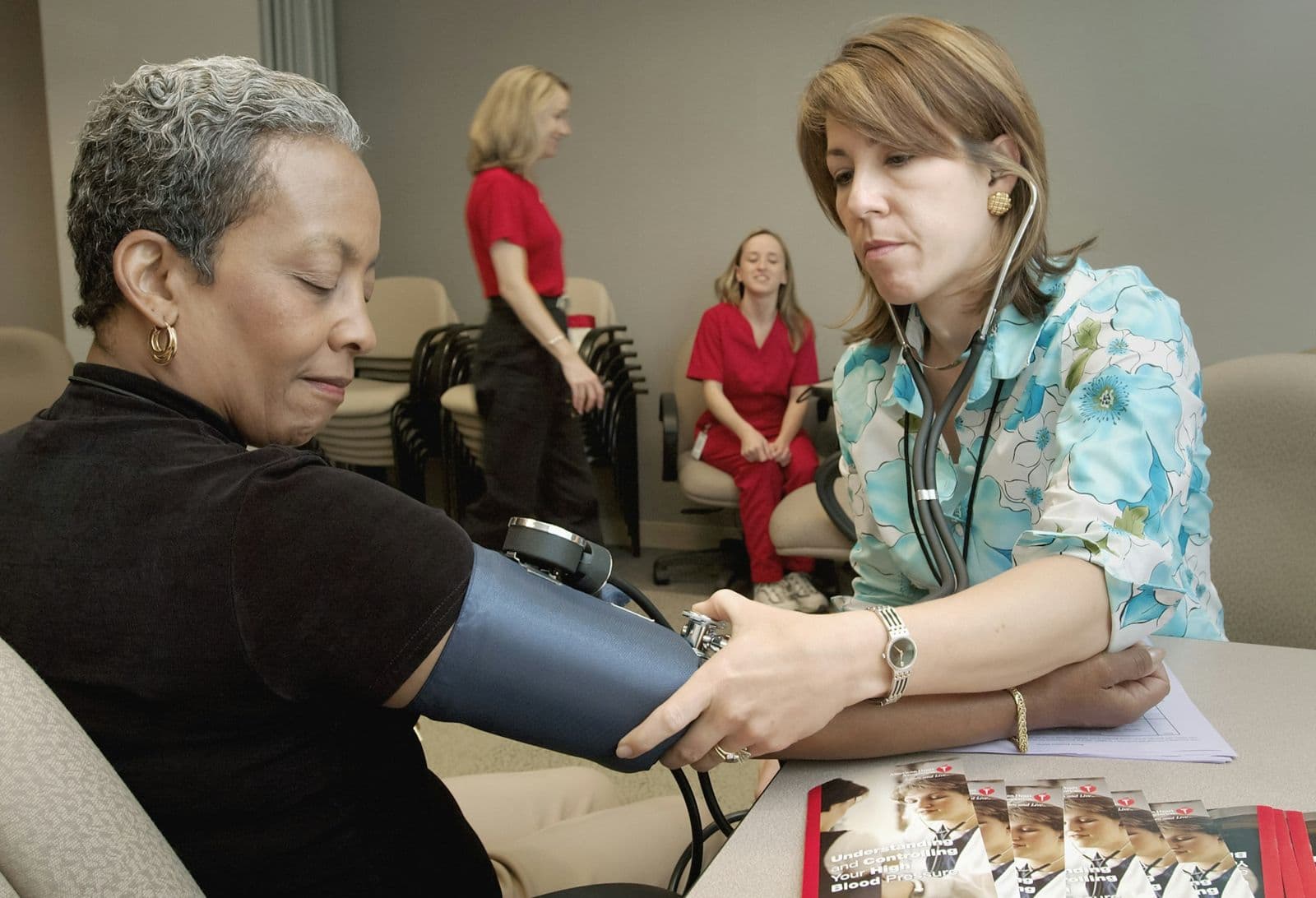 A nurse checks a woman's blood pressure at a table during a clinic visit.