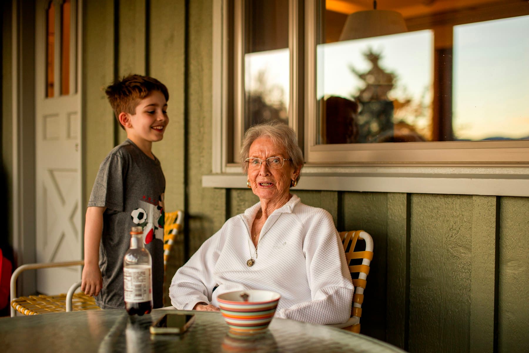 A child standing beside an older woman at a porch table