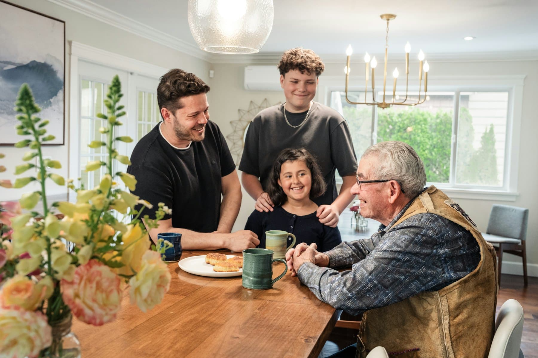 A family gathered around a wooden dining table with mugs and pastries