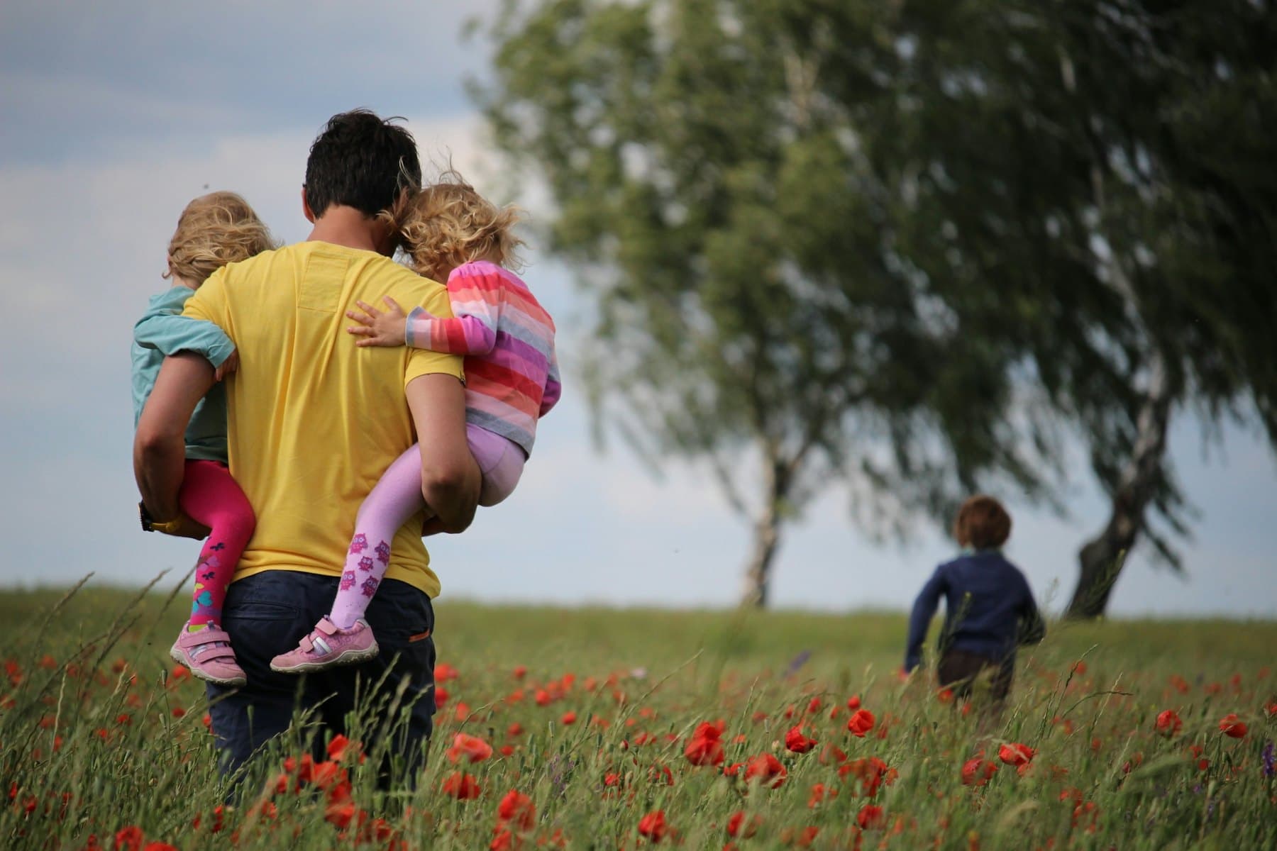 A man carrying two girls through a field of flowers
