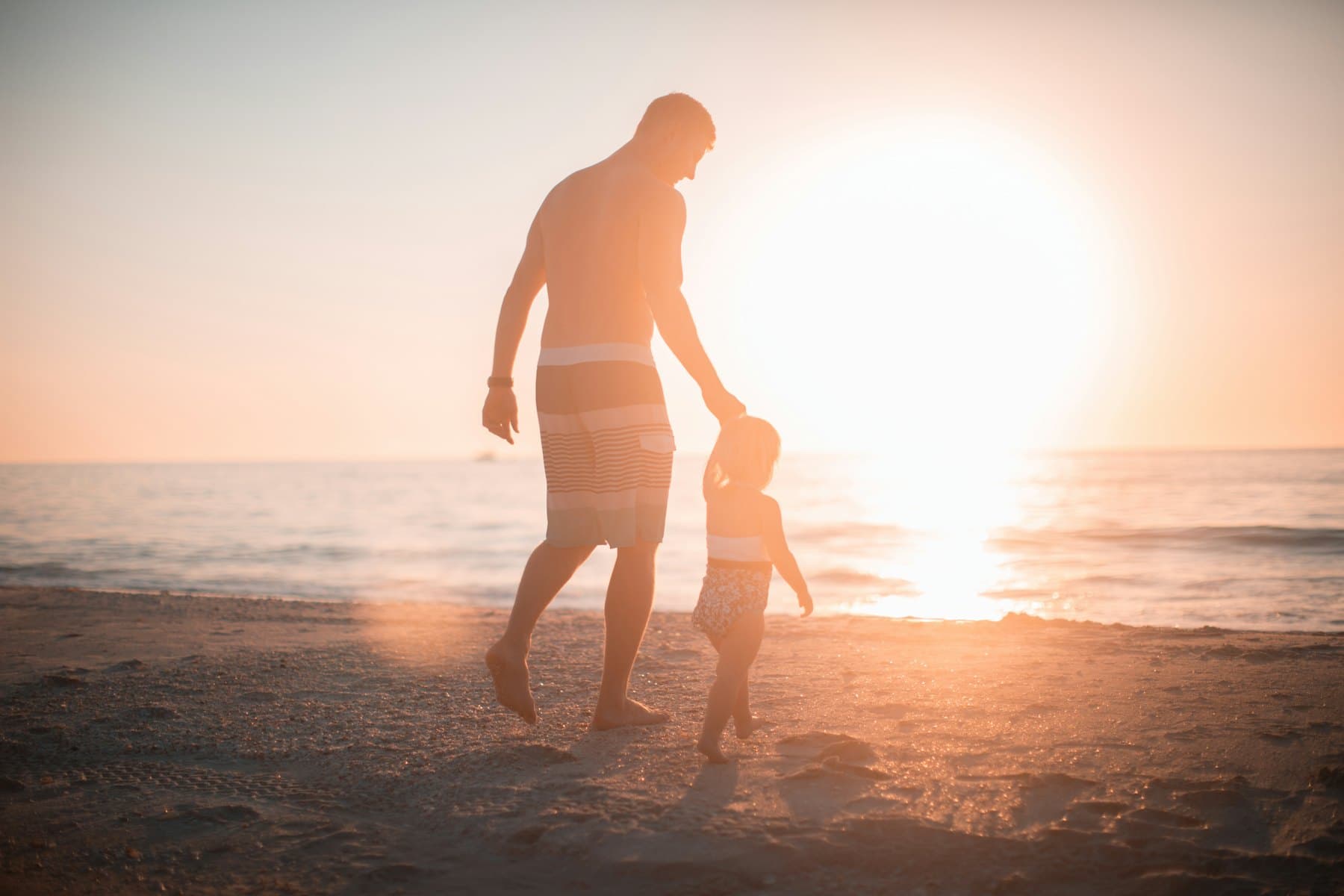 A man holding a girl as they walk toward the sea