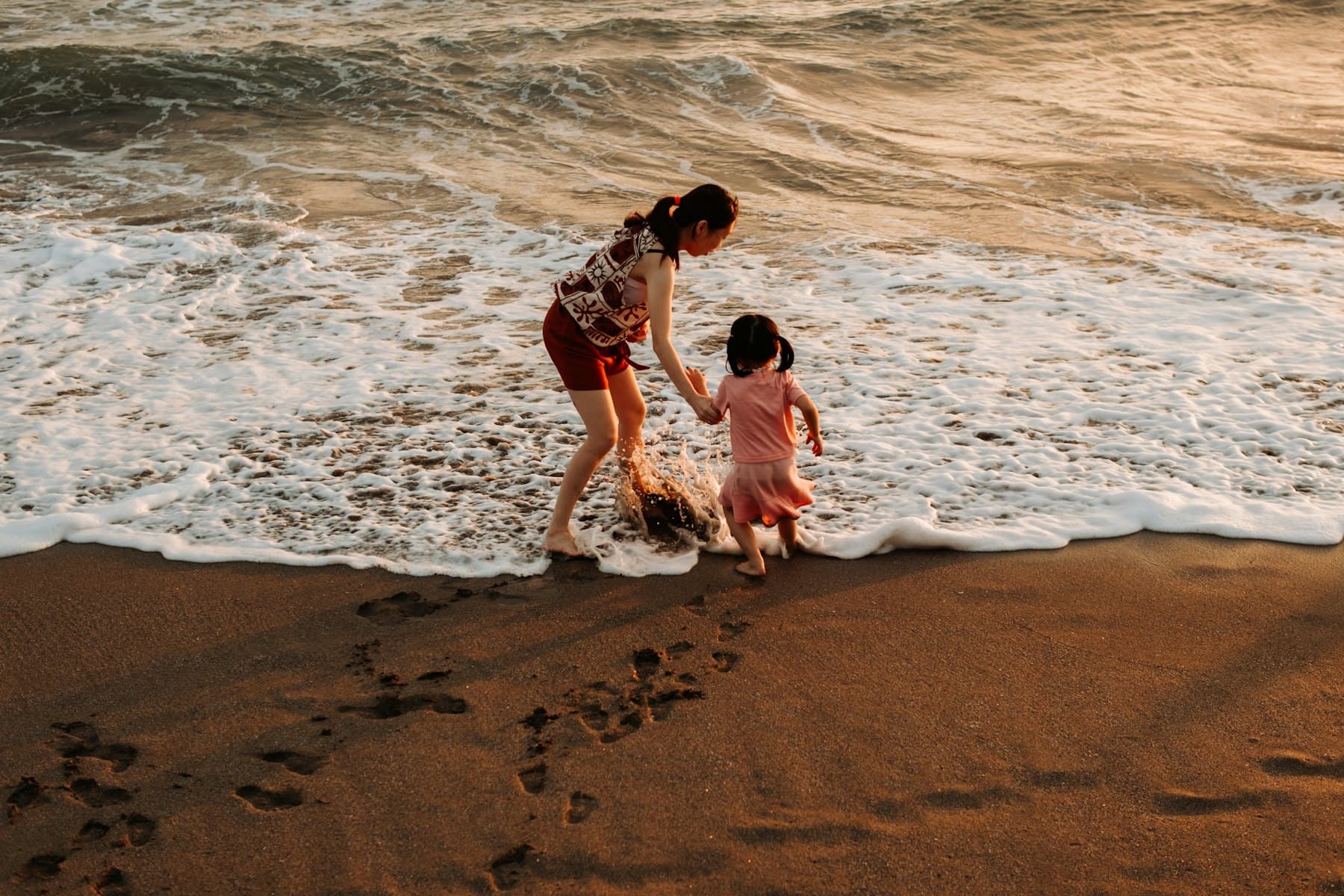 A mother and child walking on a beach at sunset