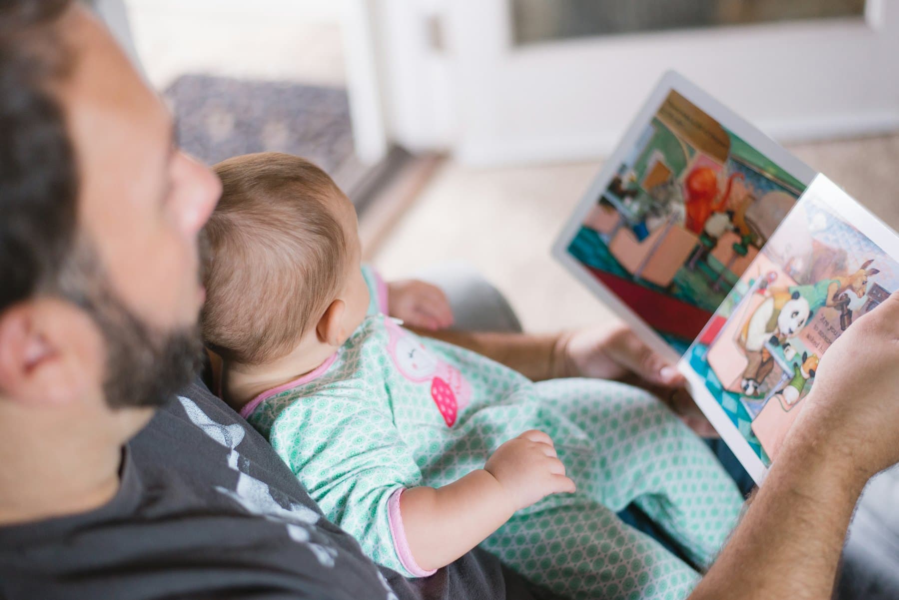 A person holding a baby while reading a book
