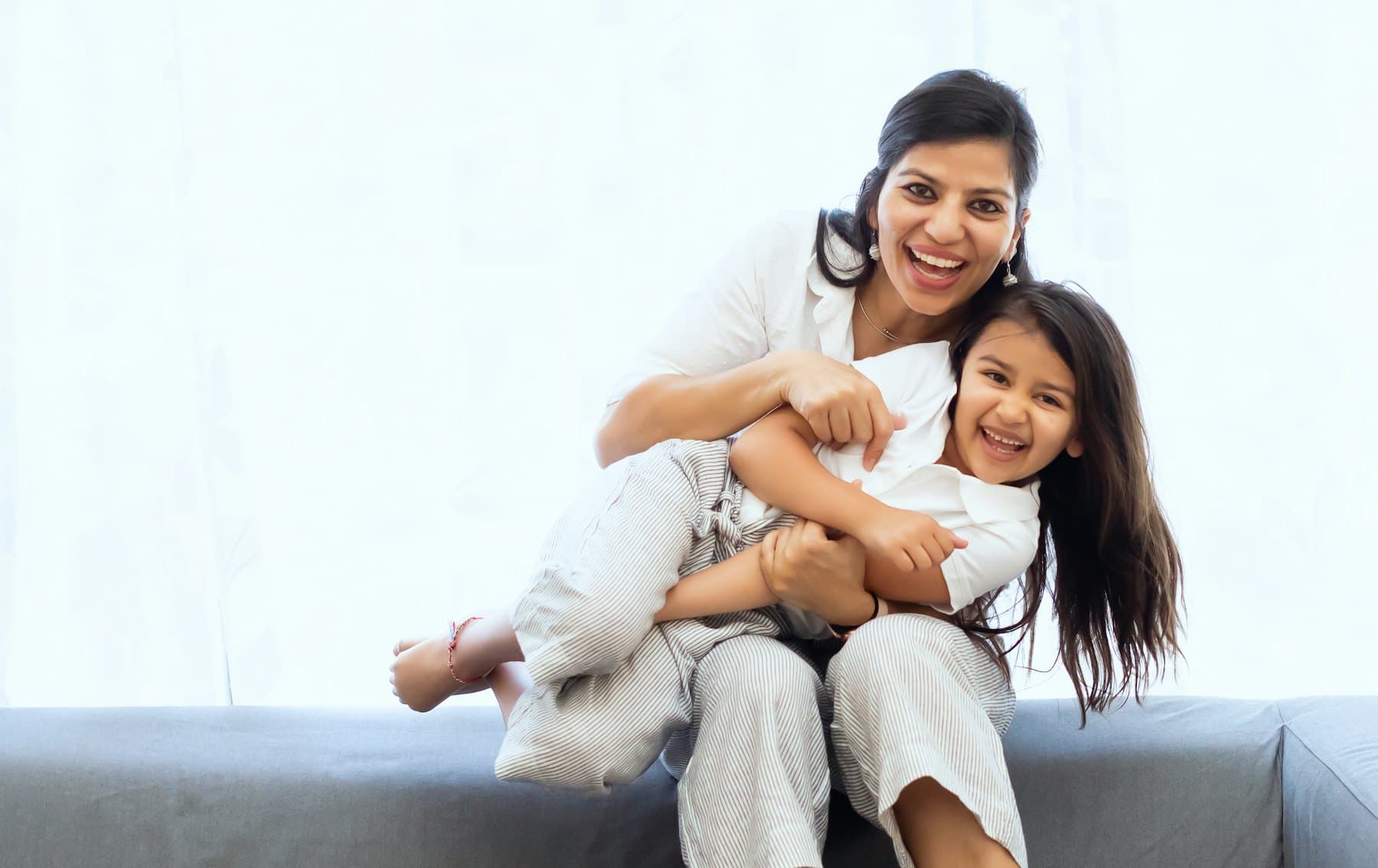 A woman holding a laughing child on a sofa