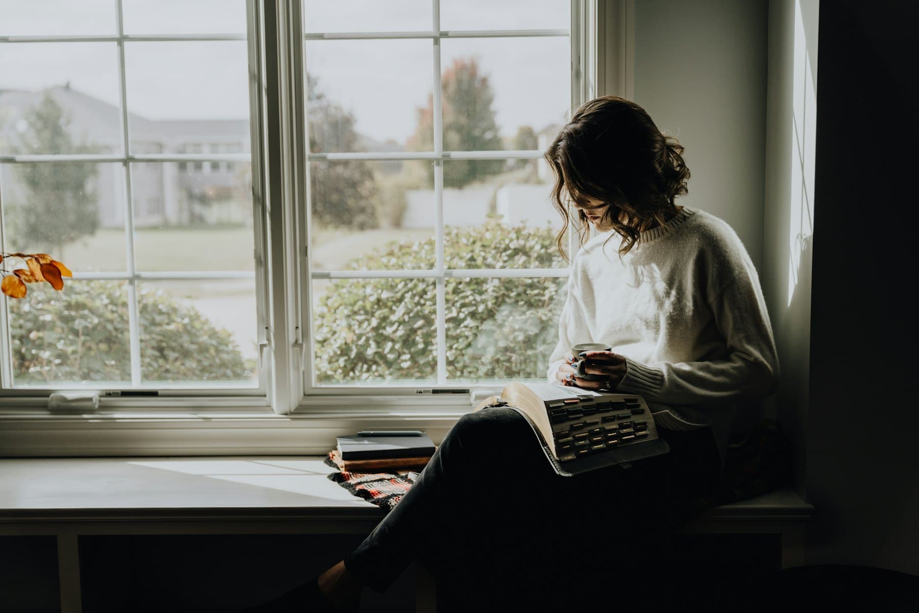 A woman holding a mug while reading a book