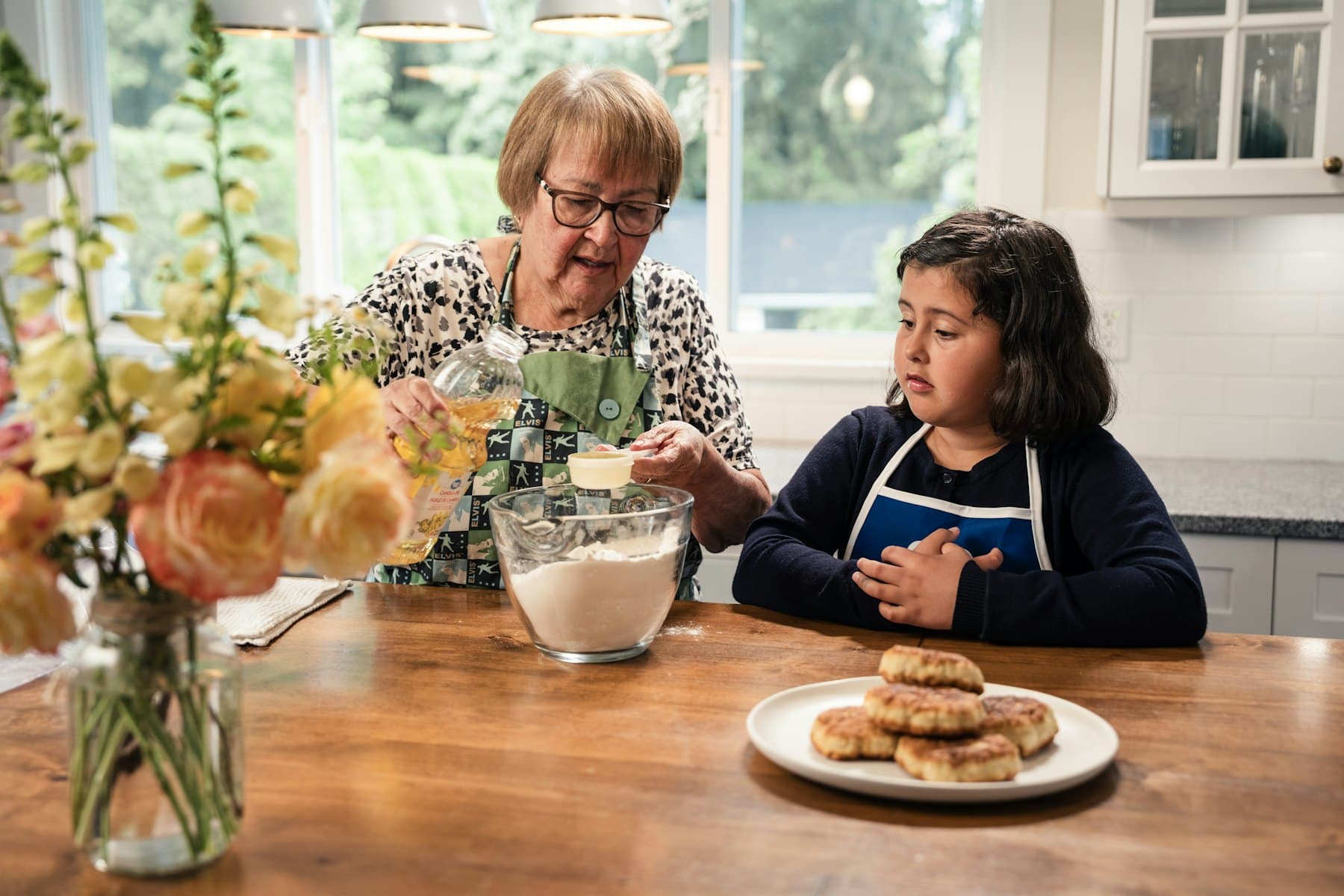 An adult and a child baking together in a sunlit kitchen