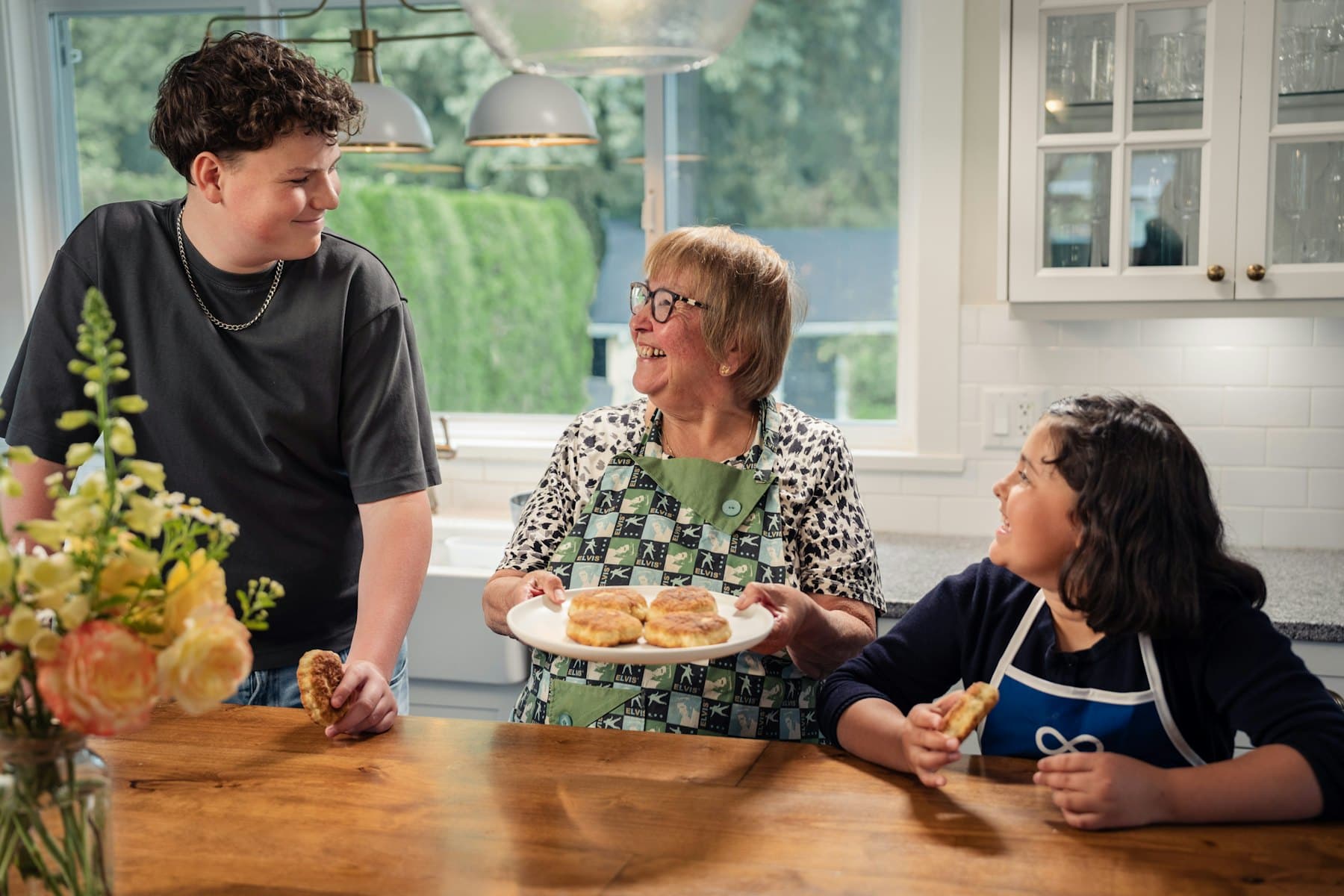 An adult and two children in a kitchen with a plate of biscuits