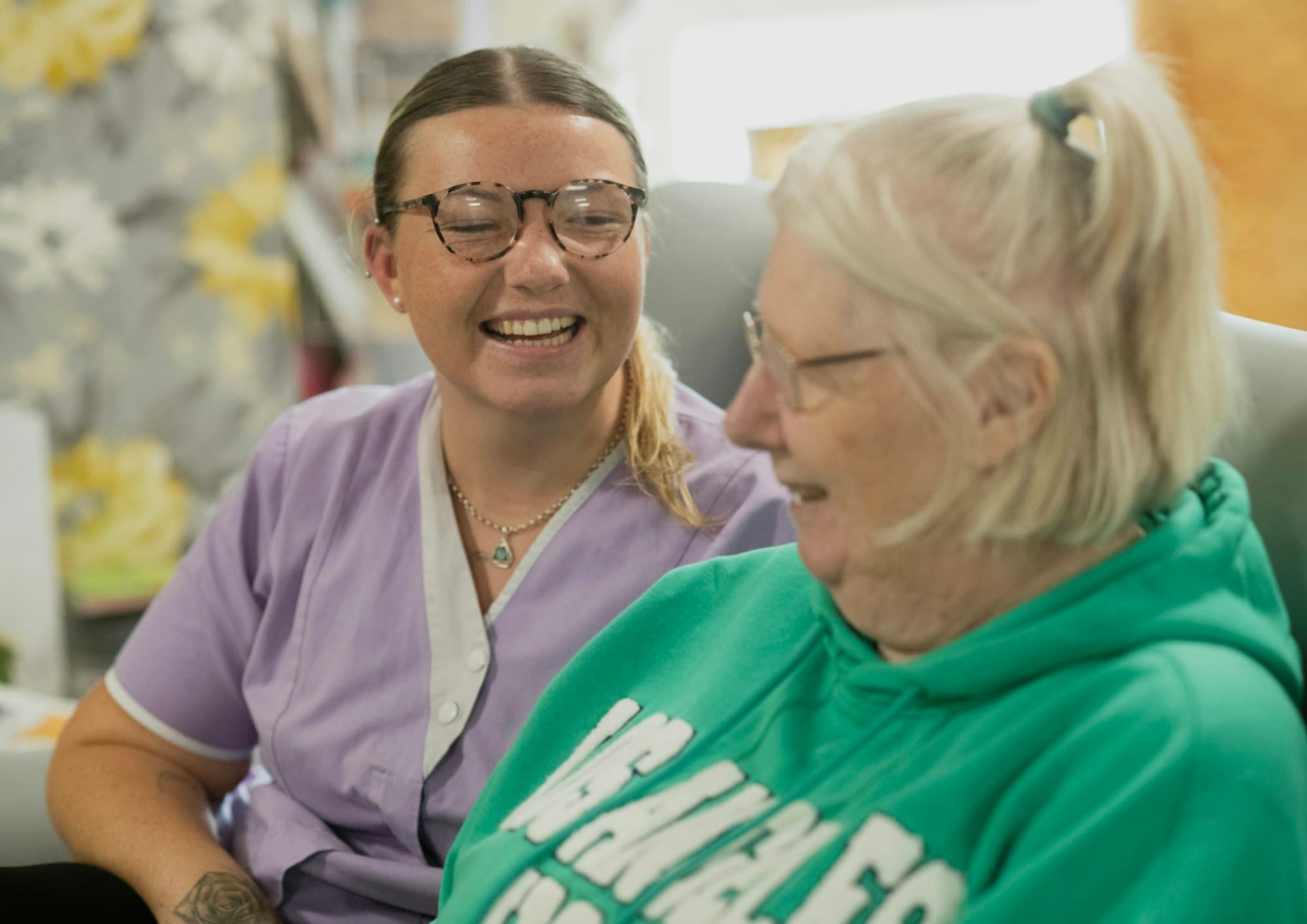 A caregiver and an older woman laughing together