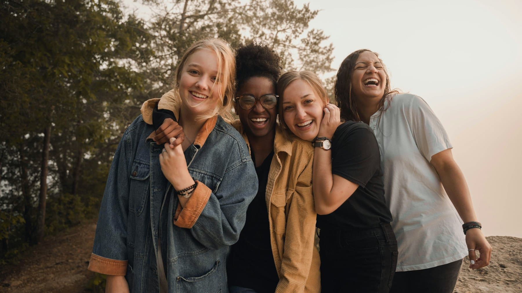 Four women laughing together outdoors at golden hour