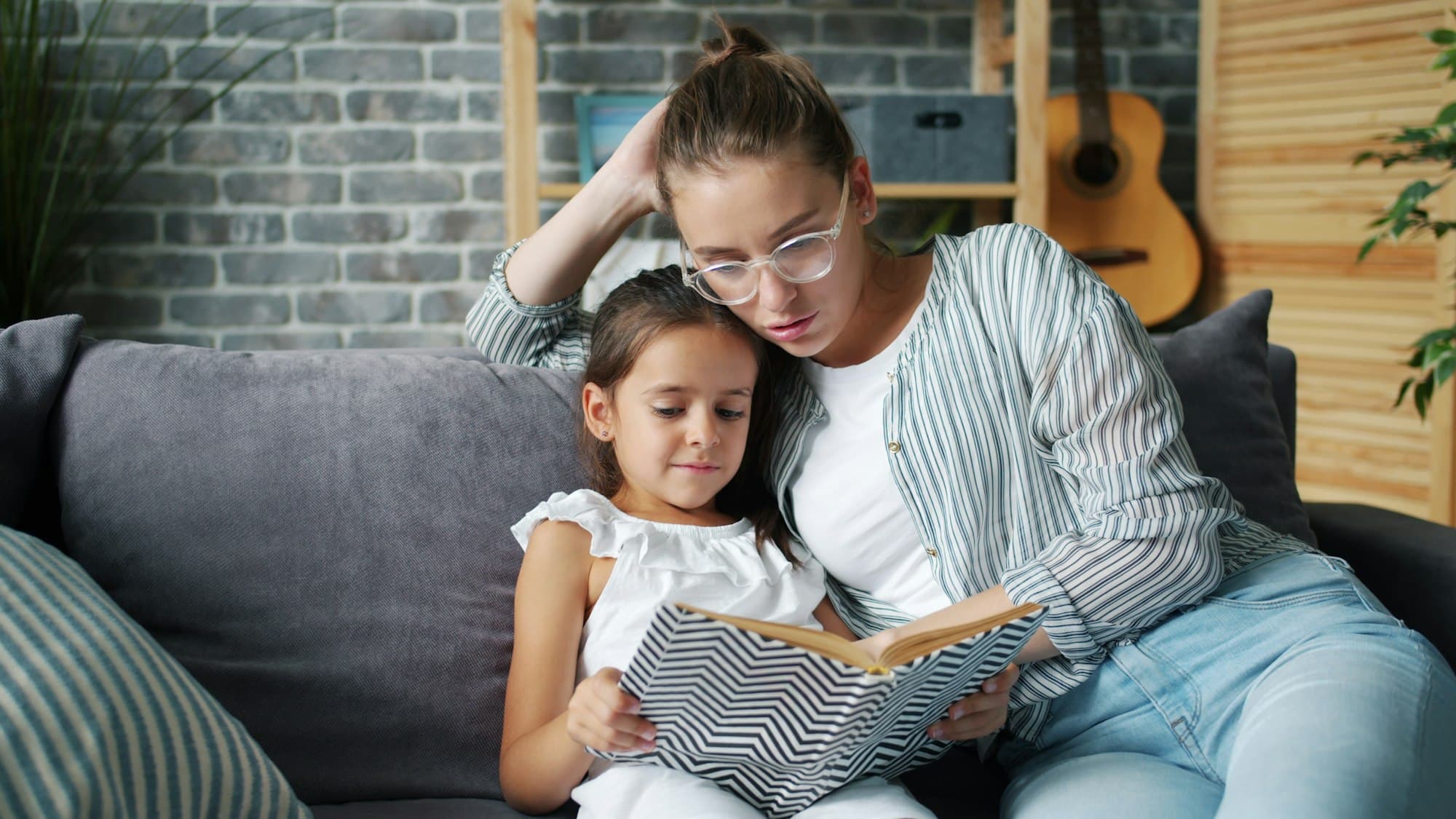 A mother and her daughter reading a book together on a couch
