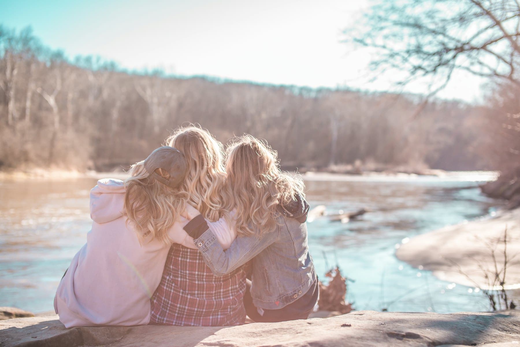 Three women sitting on a rock by the water