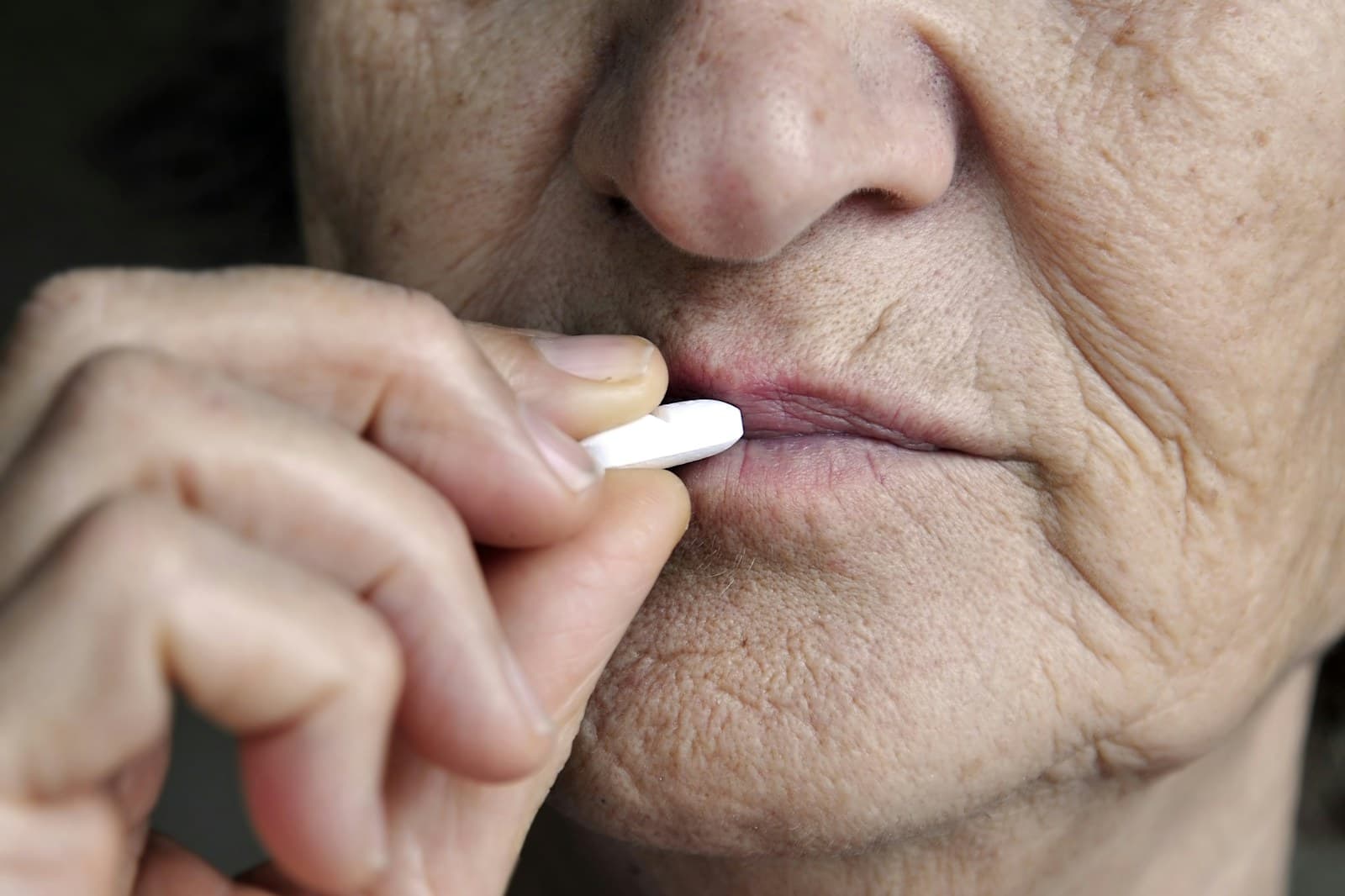 Close-up of an older woman placing a white pill between her lips.