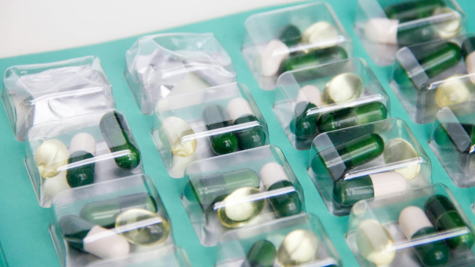 Green and white capsules sealed in clear blister packs on a teal background.
