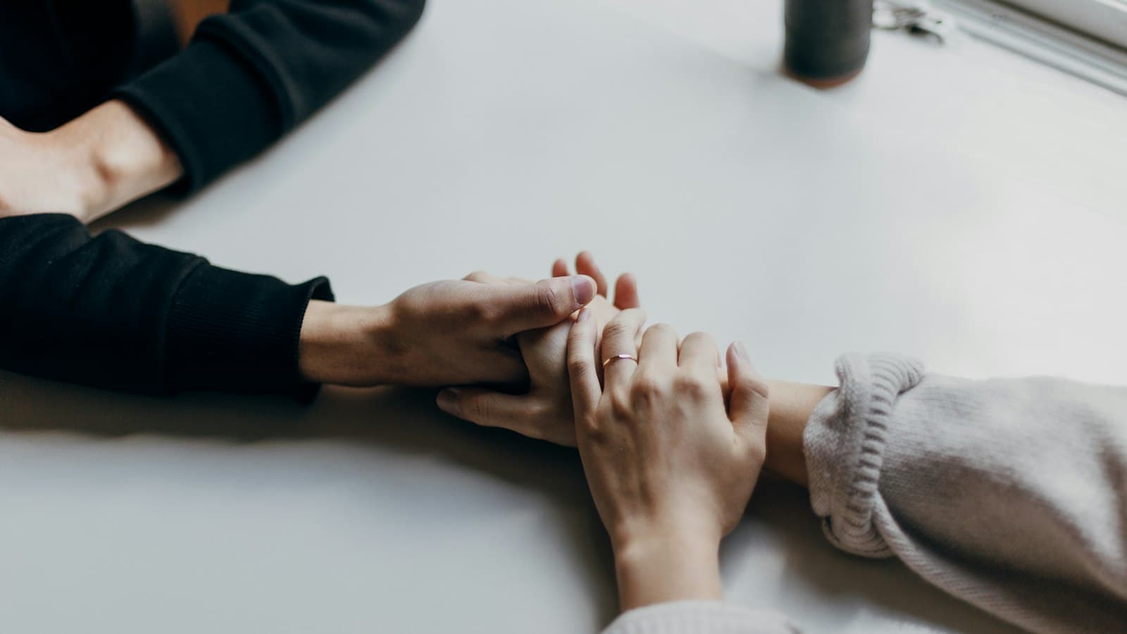 Two people holding hands in comfort, one resting a hand on the other's.