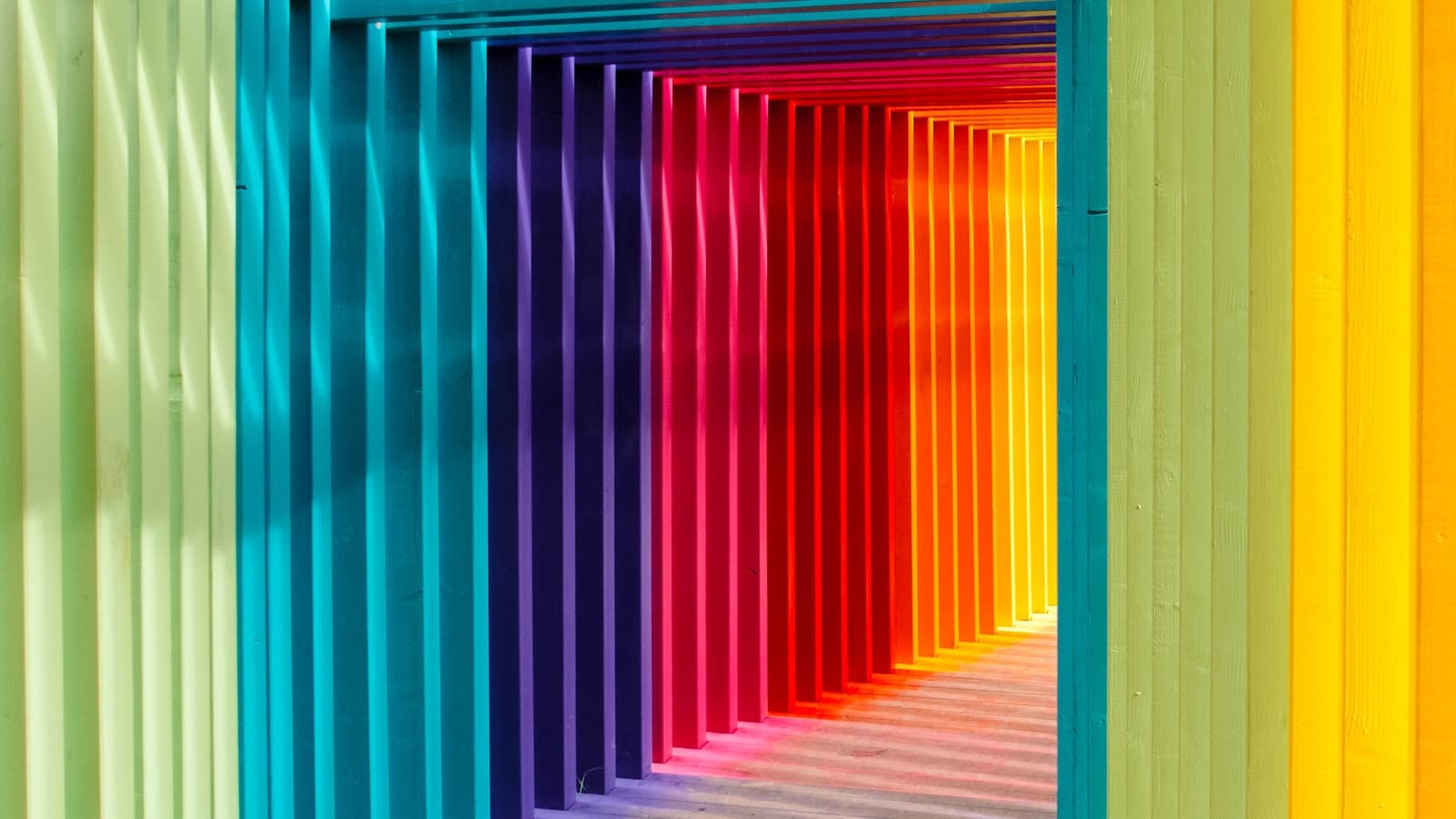 Layered passage of colorful vertical slats forming a tunnel of overlapping hues, representing how multiple rare conditions stack and interconnect into a single complex clinical picture