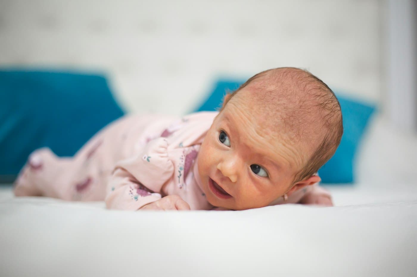 A newborn lying on his stomach and lifting his head to look to the side.