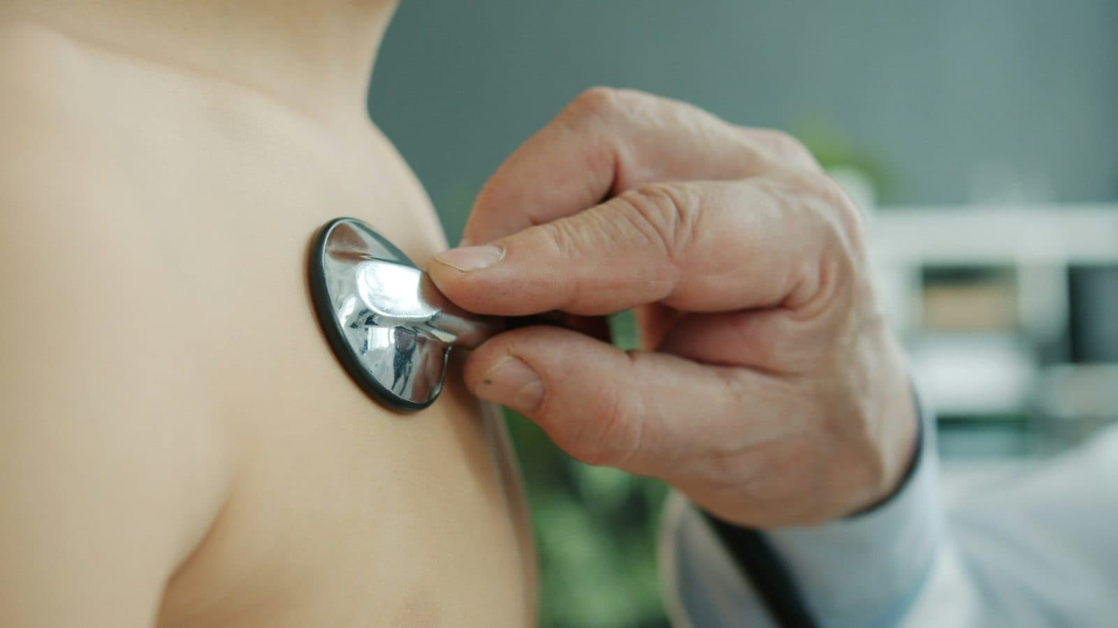 A doctor presses a stethoscope to a patient's chest to listen to their breathing.