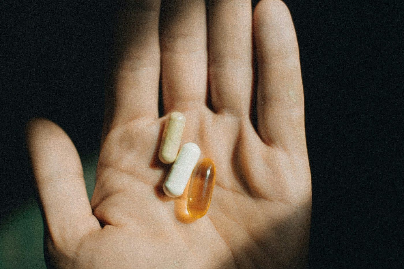 An open palm holding 3 different capsules against a dark background.