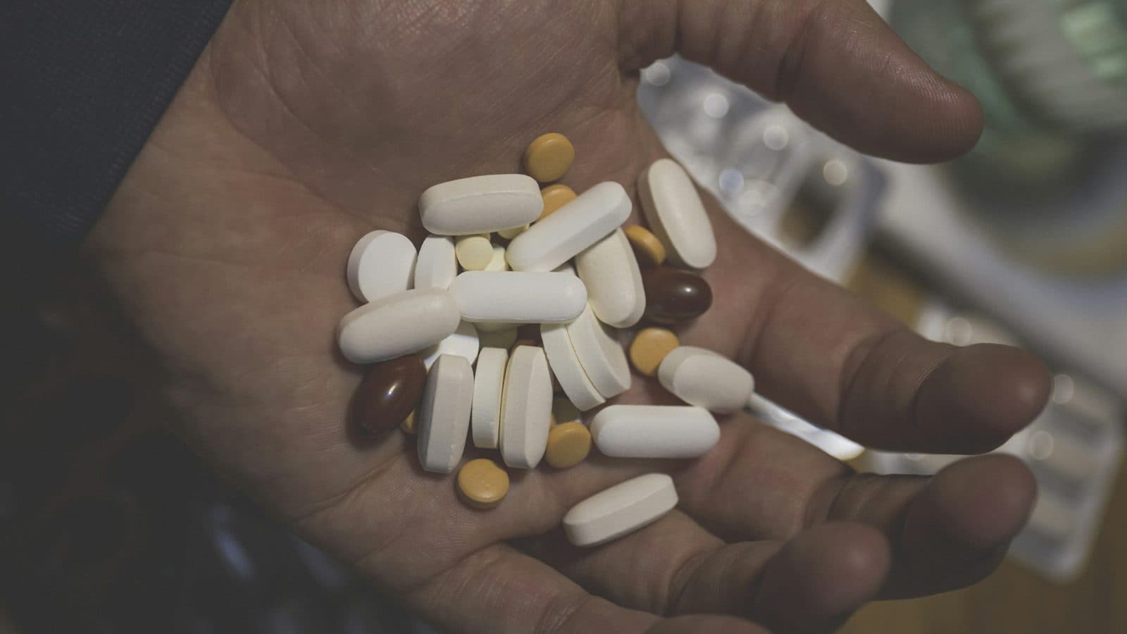 A handful of white, yellow and brown pills in the open palm of a person's hand.
