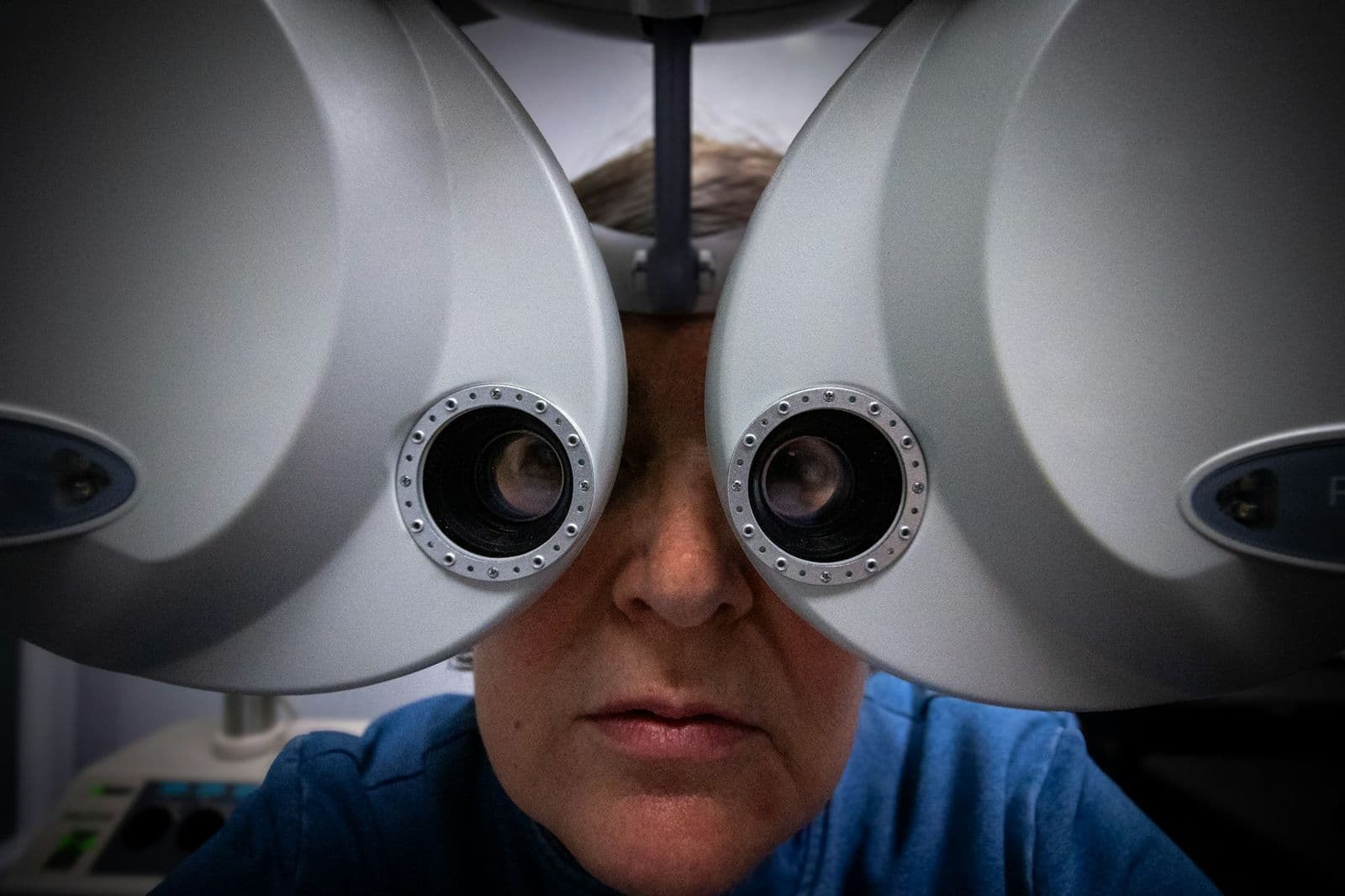 A woman looks into the lenses of an eye exam machine at an eye doctor's office.