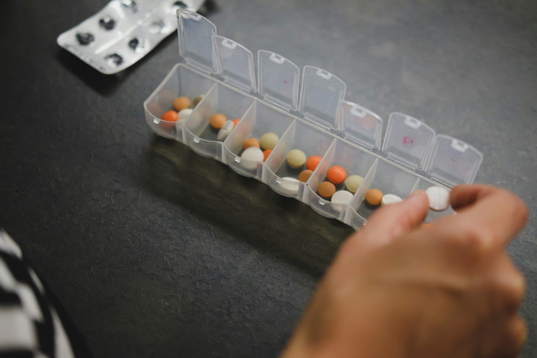 A hand reaching into a weekly pill organizer to take the day's medicine.