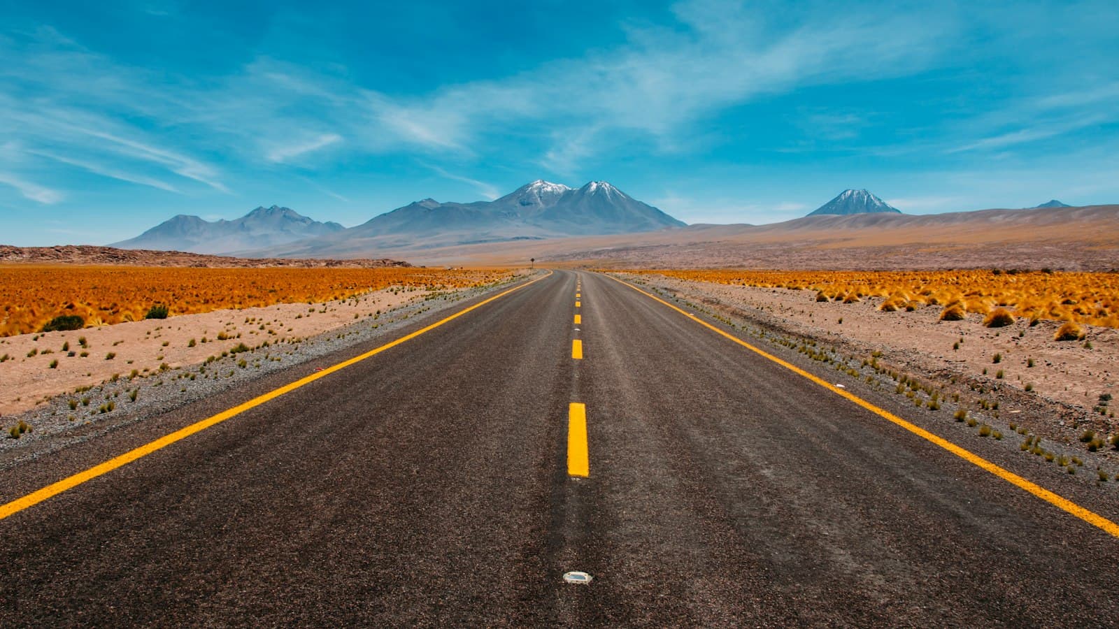 Empty two-lane desert highway running straight toward distant mountains.