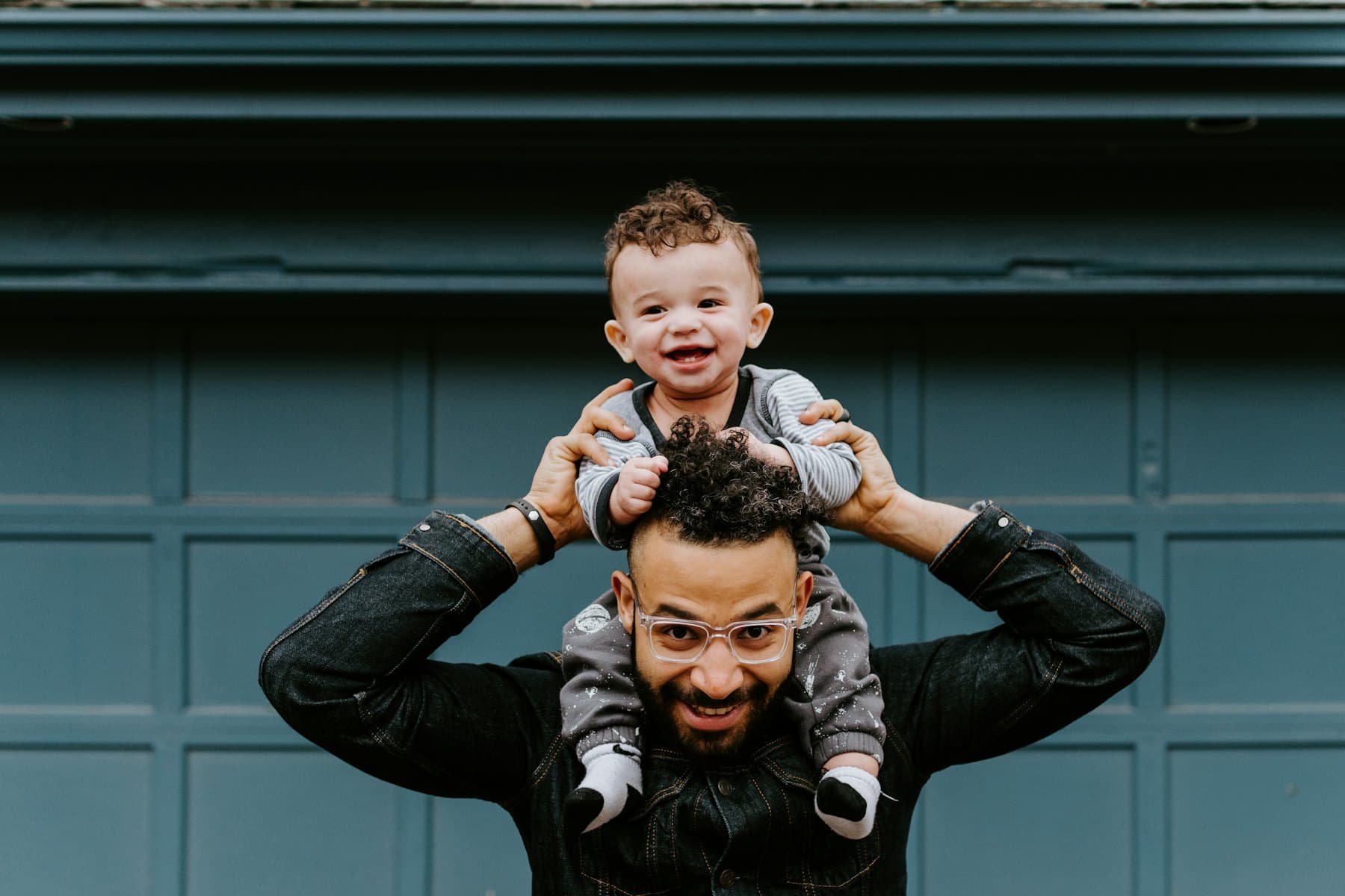 A man carrying a baby on his shoulders by a blue door