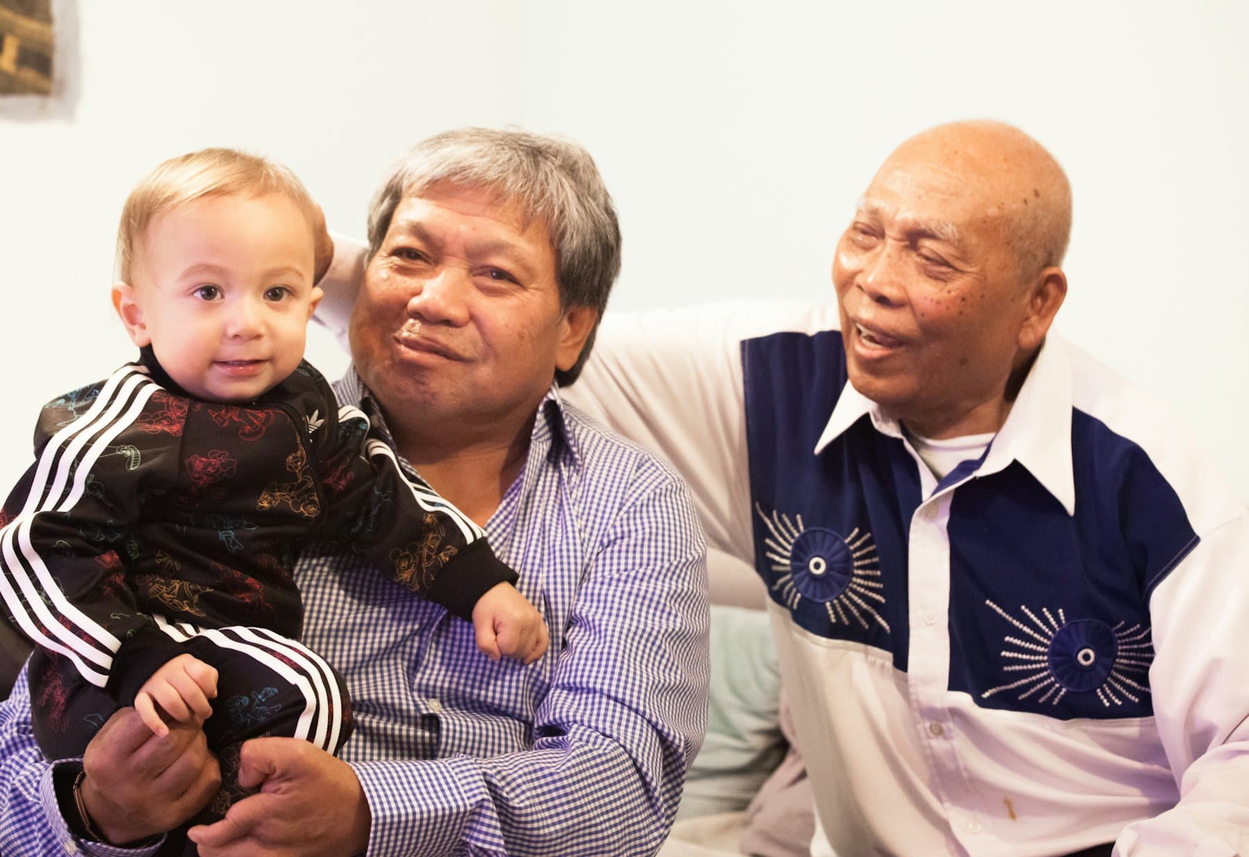 An older man holding a baby beside another man