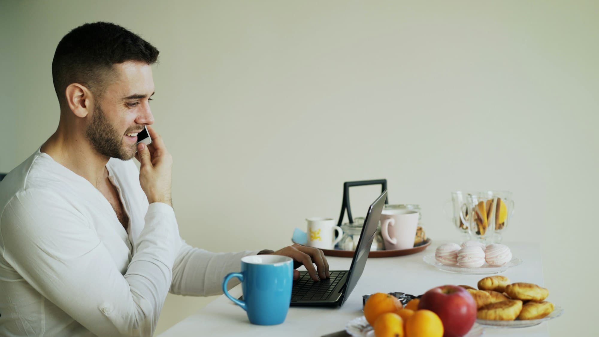 A man on a phone call with his laptop open at the table