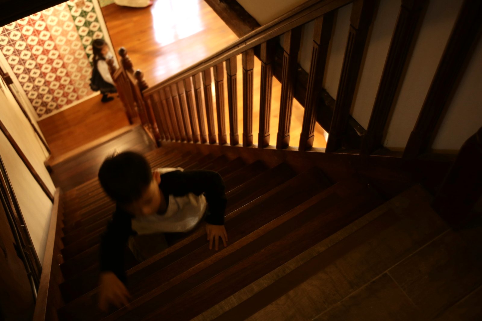 A young boy climbs a wooden staircase on his hands and feet while his sister watches from below.