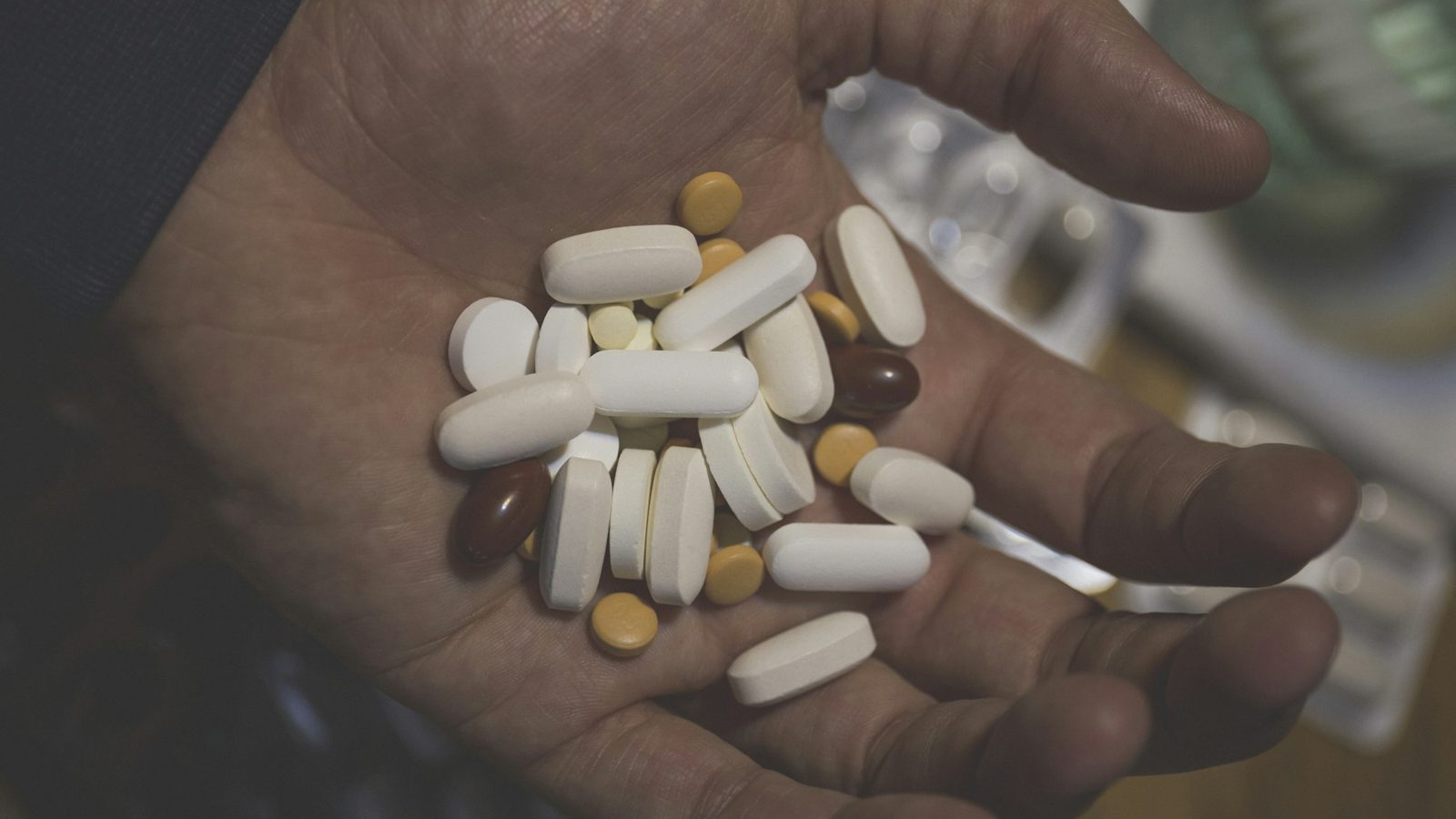 A handful of white, yellow and brown pills in the open palm of a person's hand.