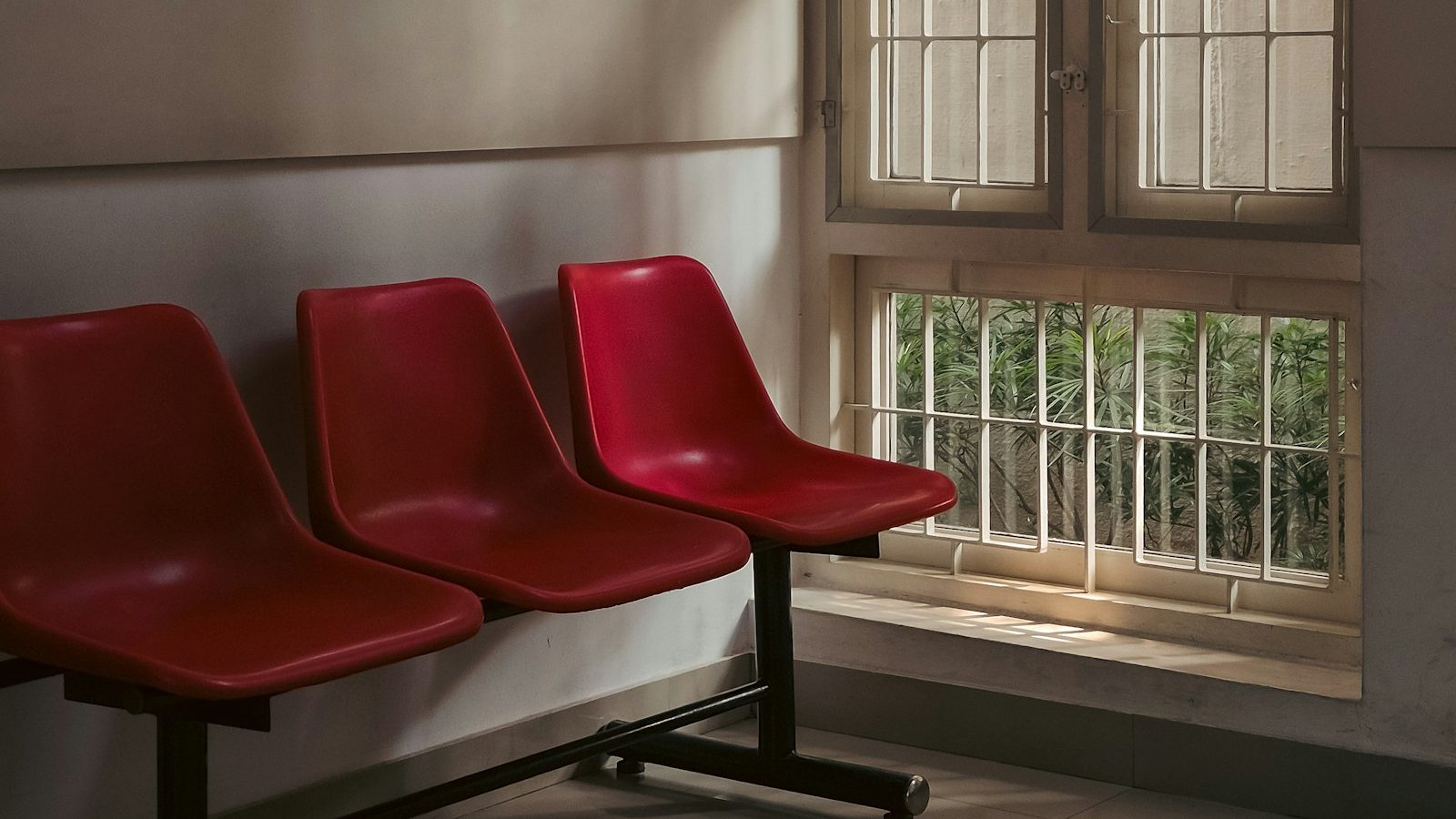 Three empty red chairs in a clinic waiting room beside a sunlit window, for families waiting on 11 rare disease FDA decisions in November 2026.